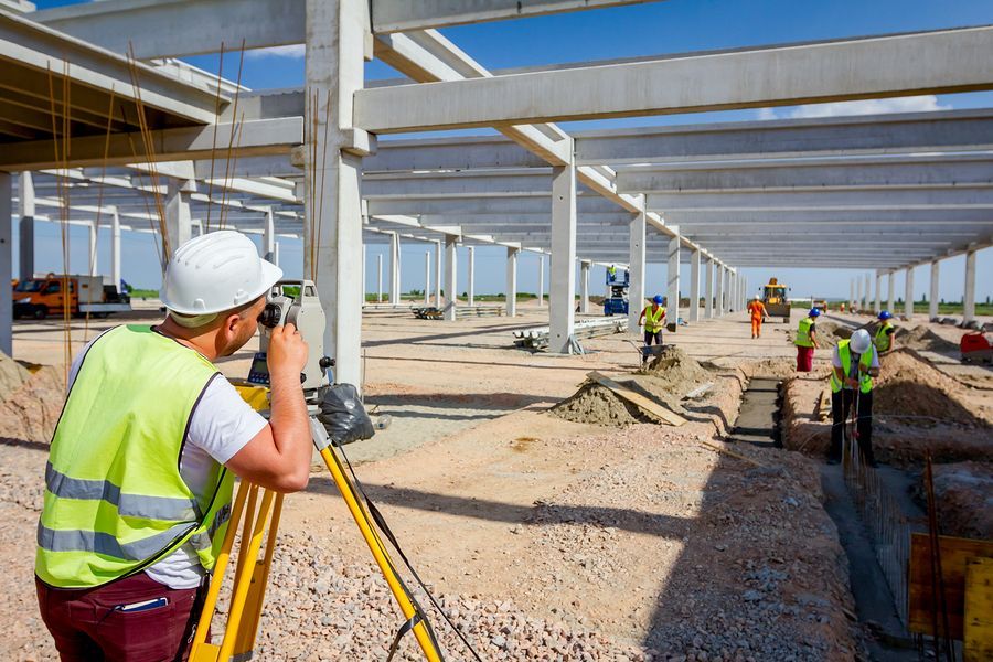 Construction worker using surveying equipment at a building site.