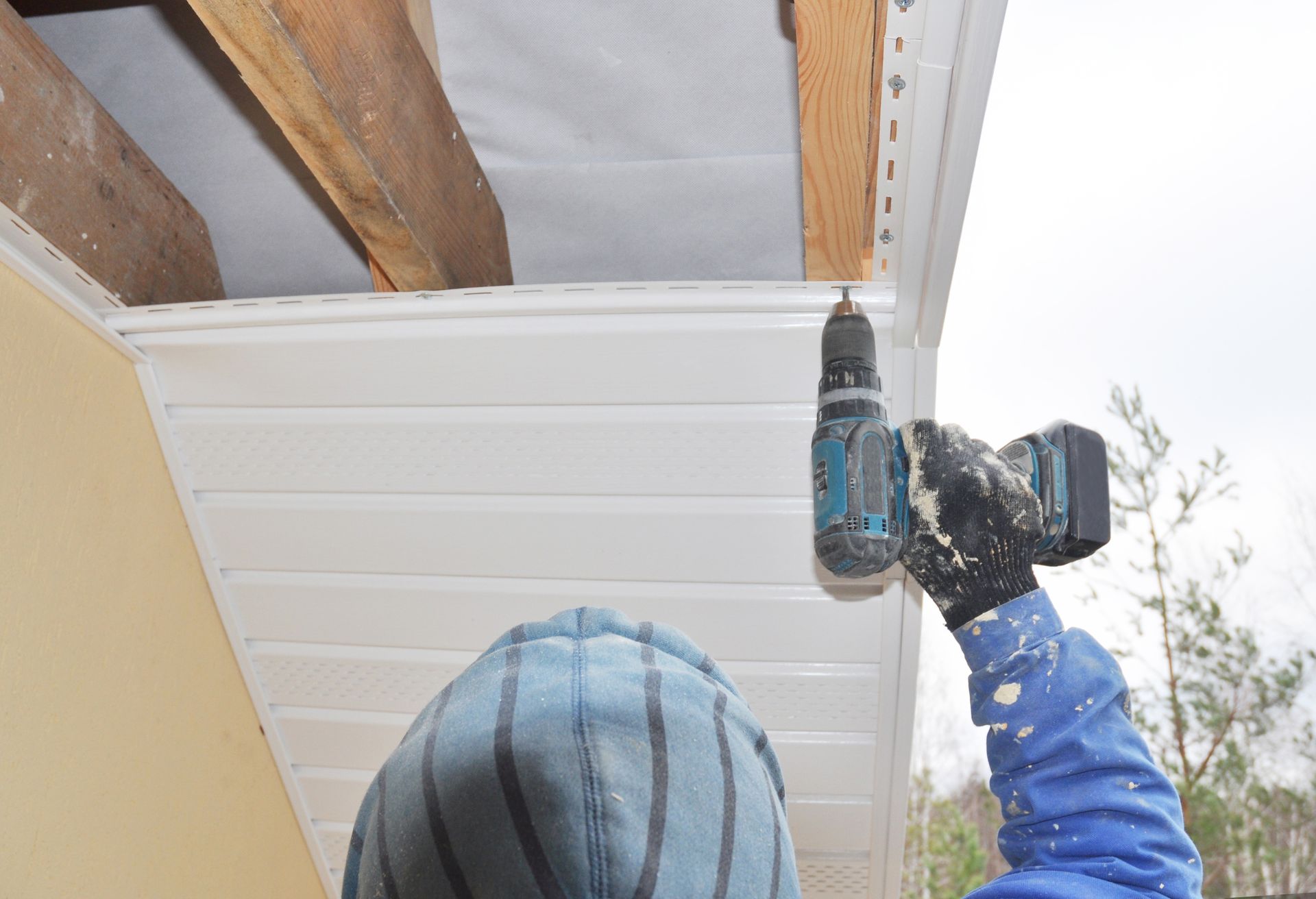 Un homme utilise une perceuse pour installer un revêtement au plafond d'une maison.