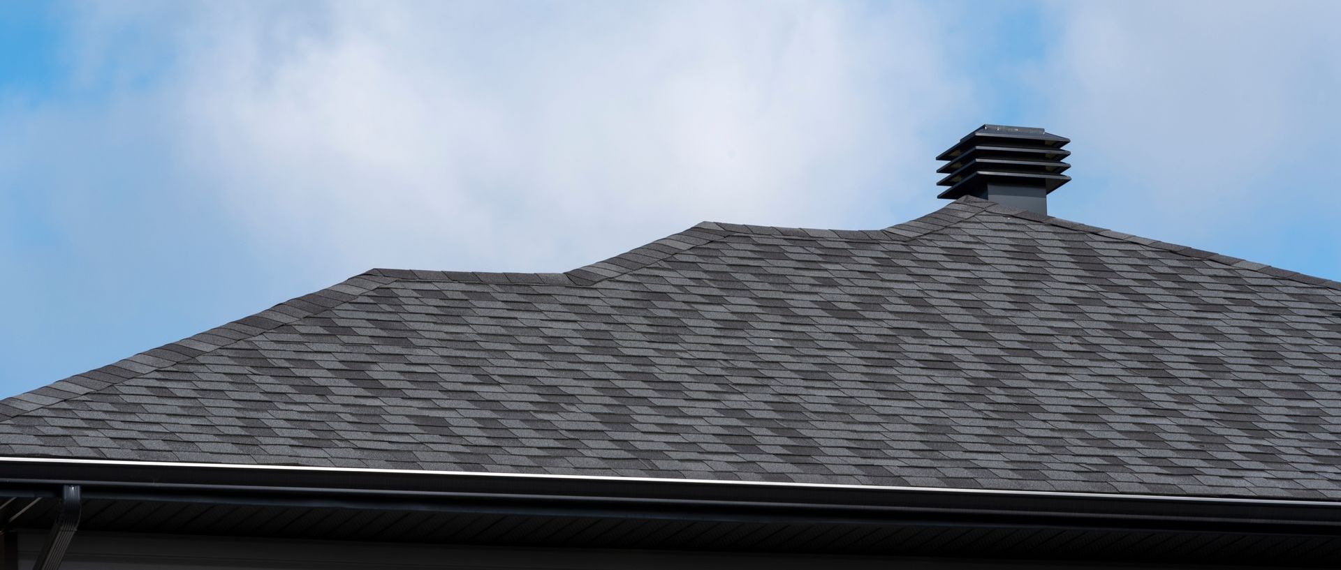 Un toit avec une cheminée au-dessus et un ciel bleu en arrière-plan.