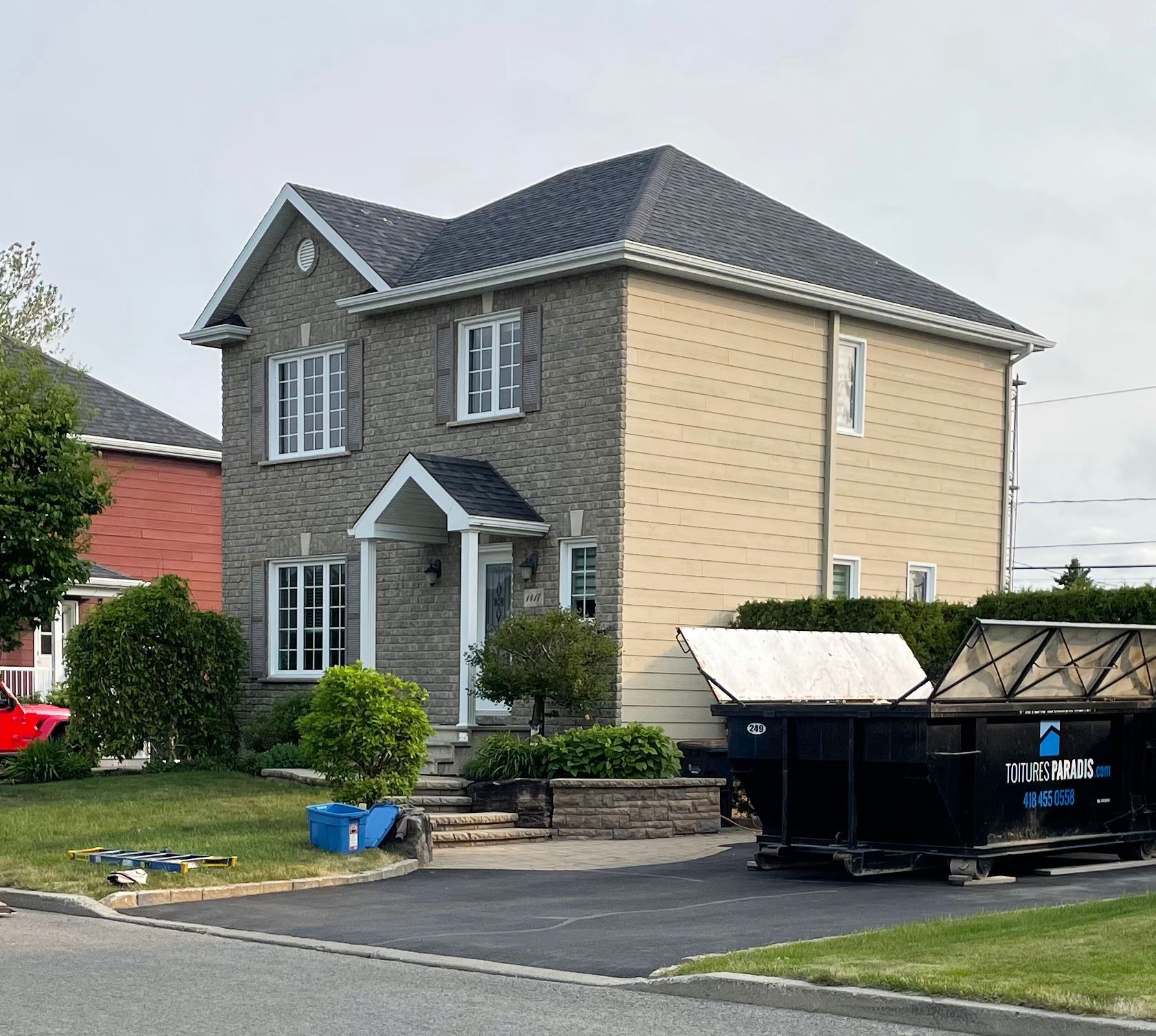 Une grande maison avec une benne à ordures devant.