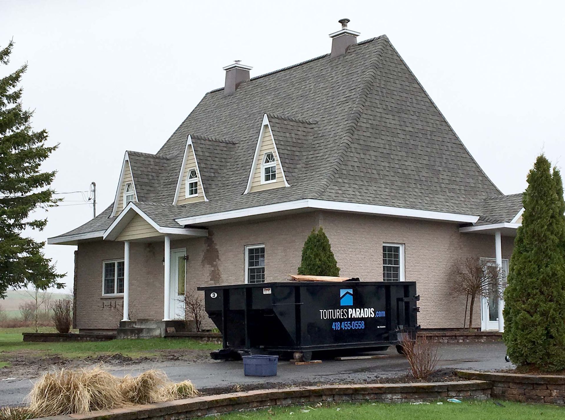 Une grande maison avec une benne à ordures devant