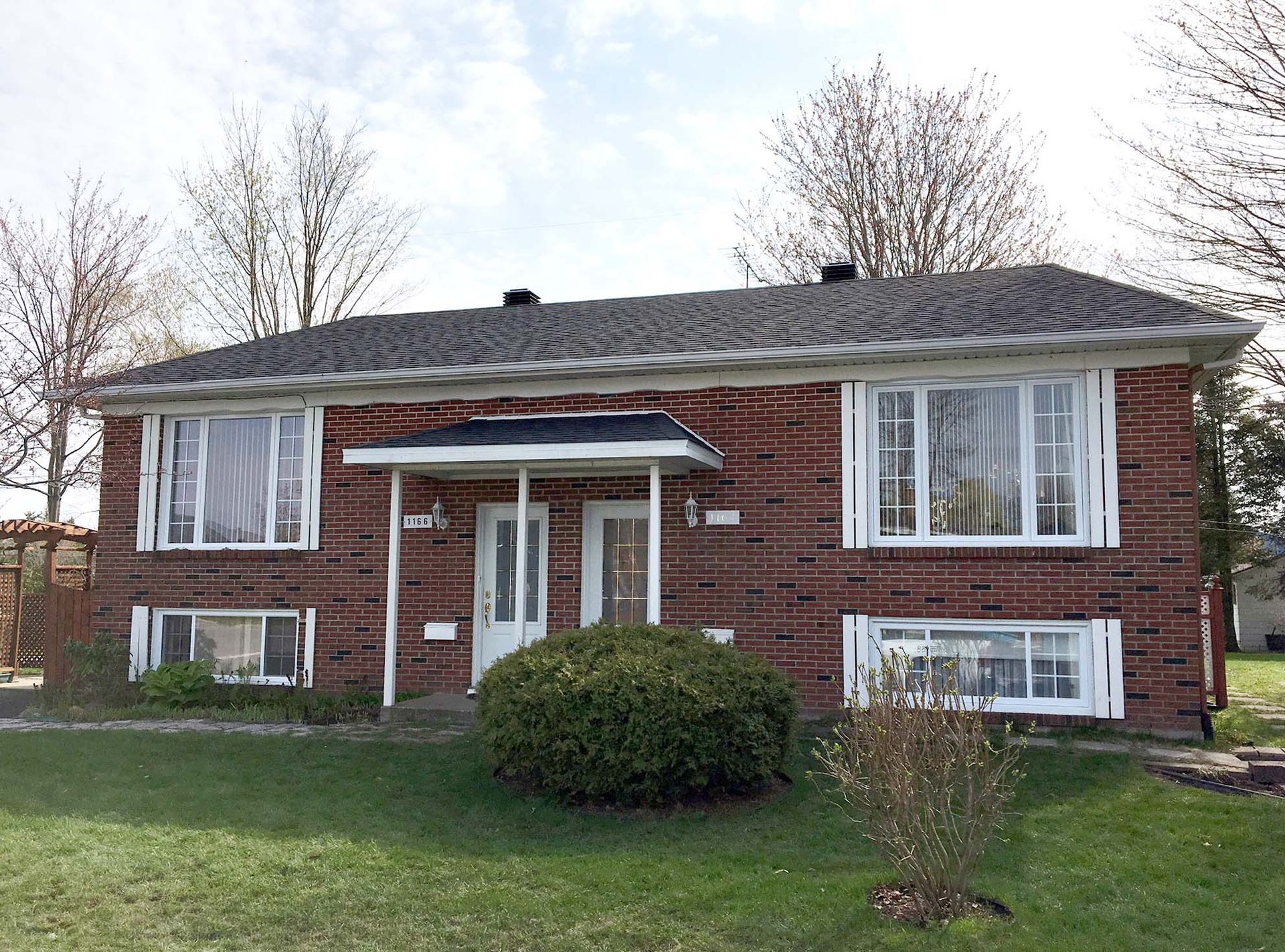 Une maison en briques avec un toit gris et des fenêtres blanches se trouve au sommet d'une pelouse verte luxuriante.