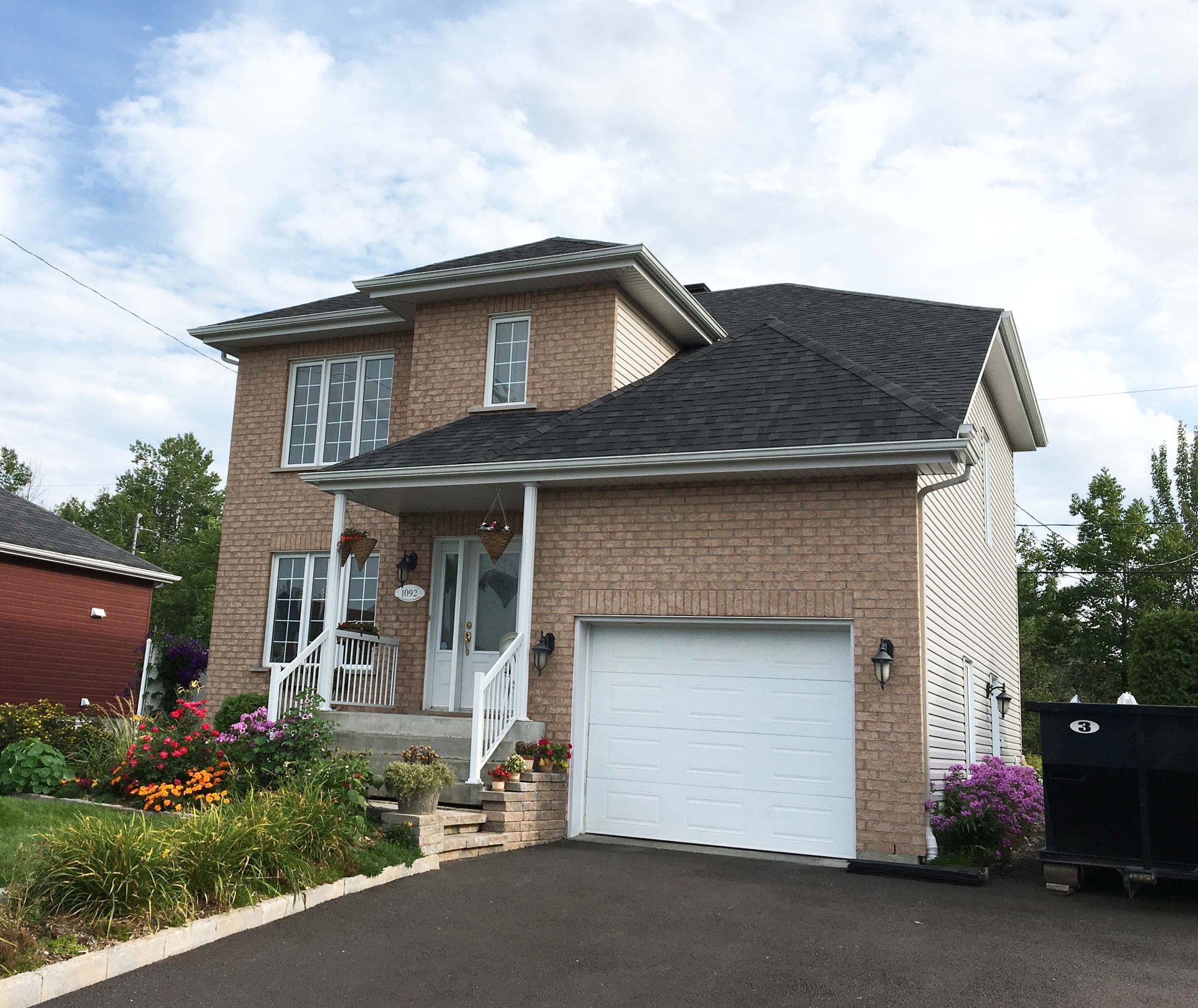 Une grande maison en briques avec un toit noir et une porte de garage blanche.