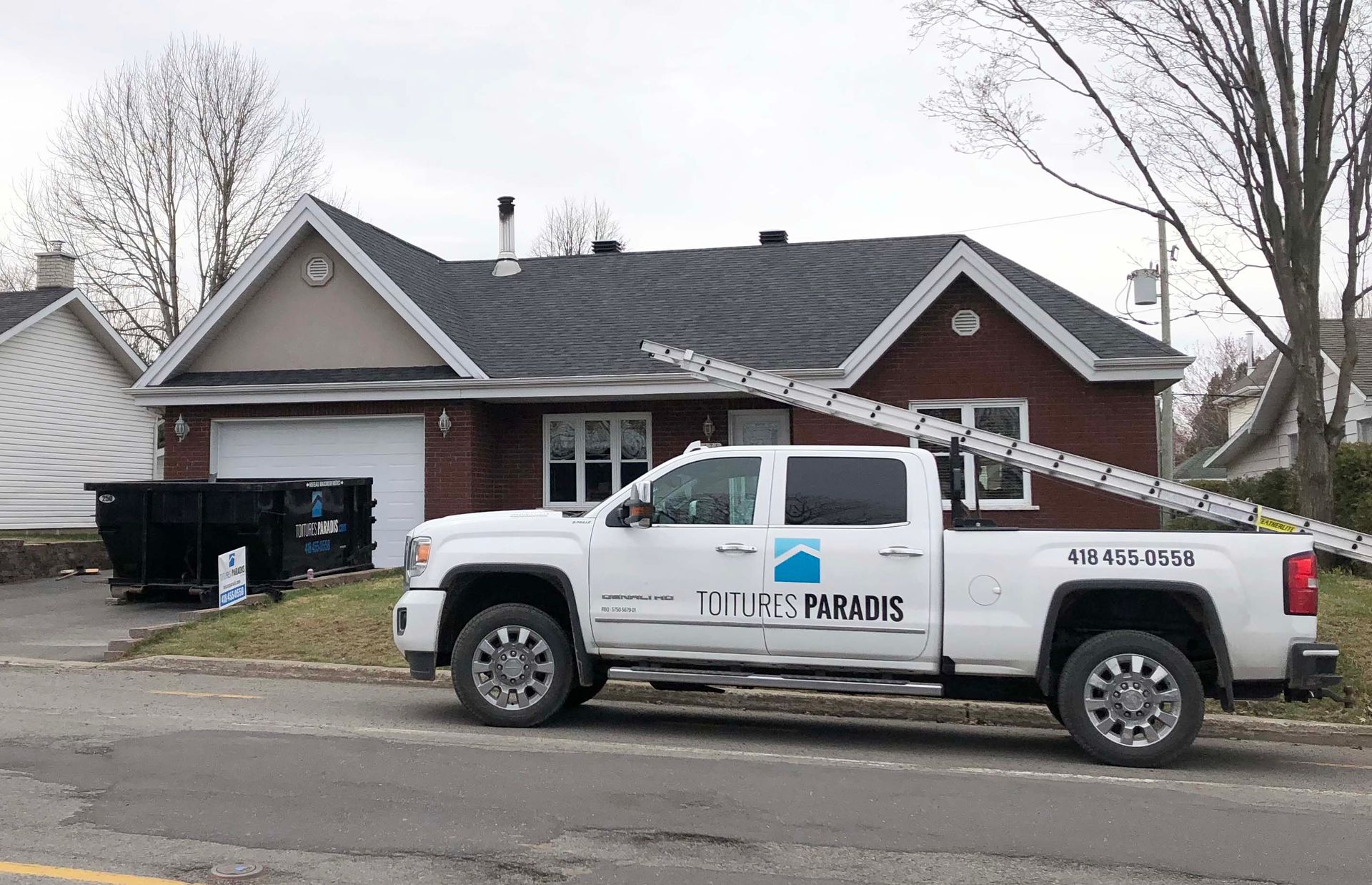 Un camion blanc avec une échelle à l'arrière est garé devant une maison.