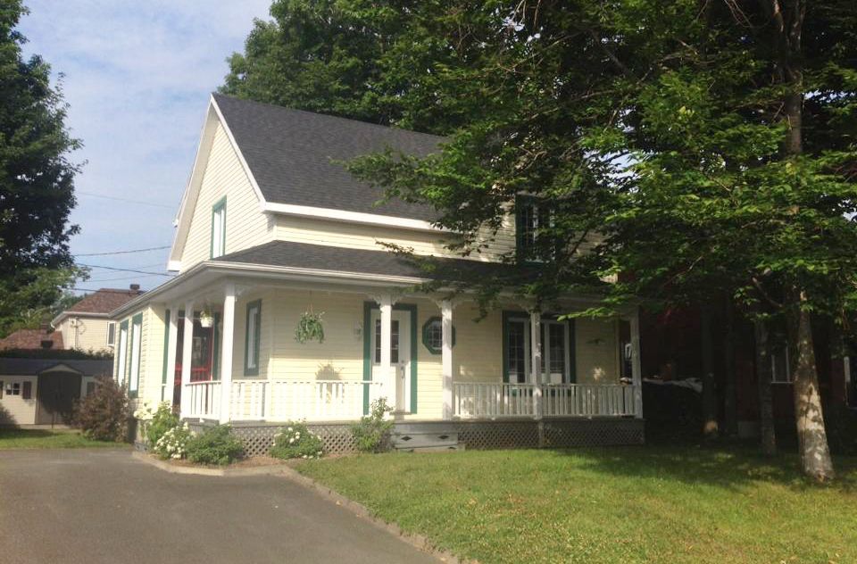 Une maison blanche avec un porche et des arbres devant