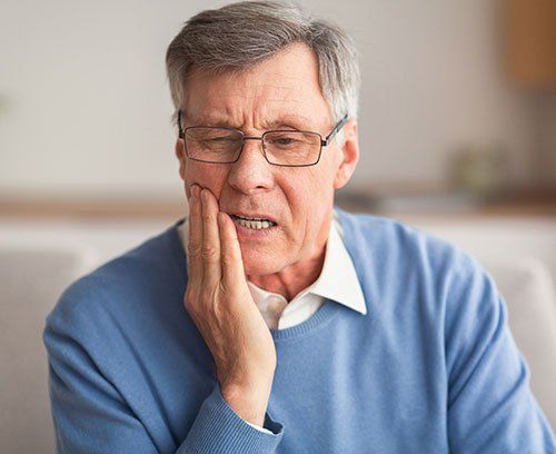 elderly man with glasses and blue shirt with hand on face