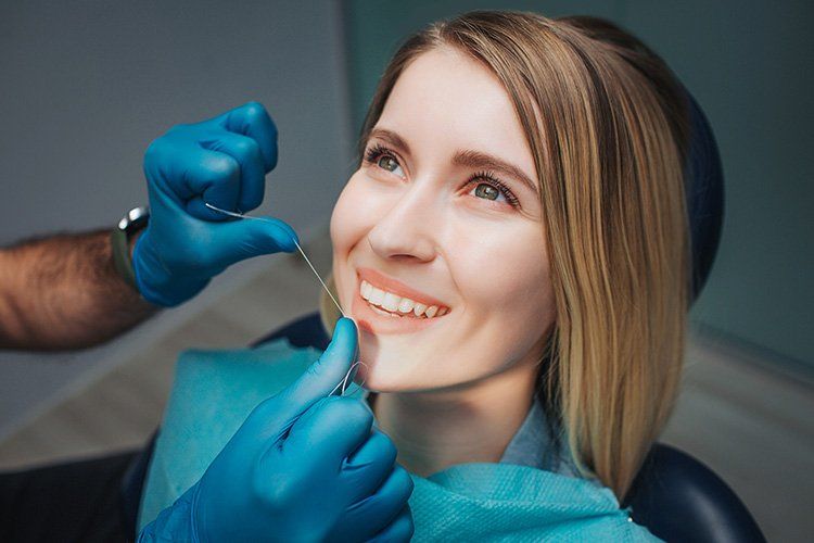A woman is sitting in a dental chair while a dentist examines her teeth.
