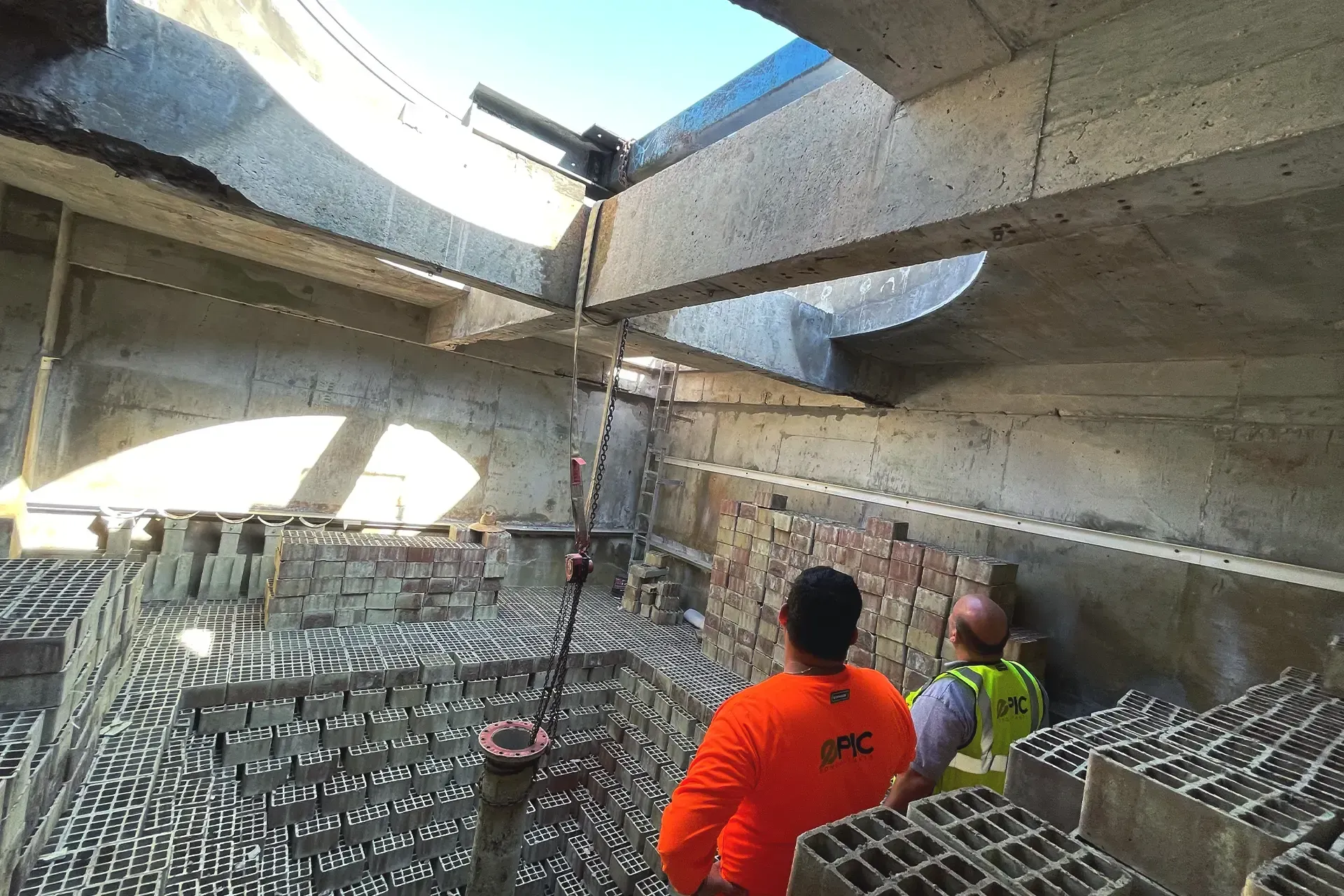 A group of construction workers are standing in a building looking up at the skylight.