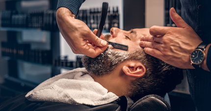 A man is getting his beard shaved by a barber in a barber shop.