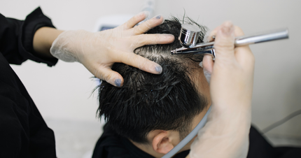 A man is getting his hair dyed by a woman in a salon.