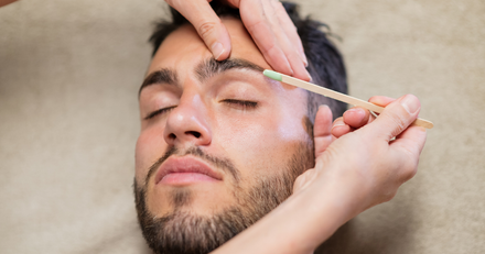 A man is getting his eyebrows waxed by a woman.