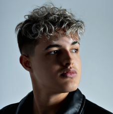 A young man with curly hair is wearing a black jacket