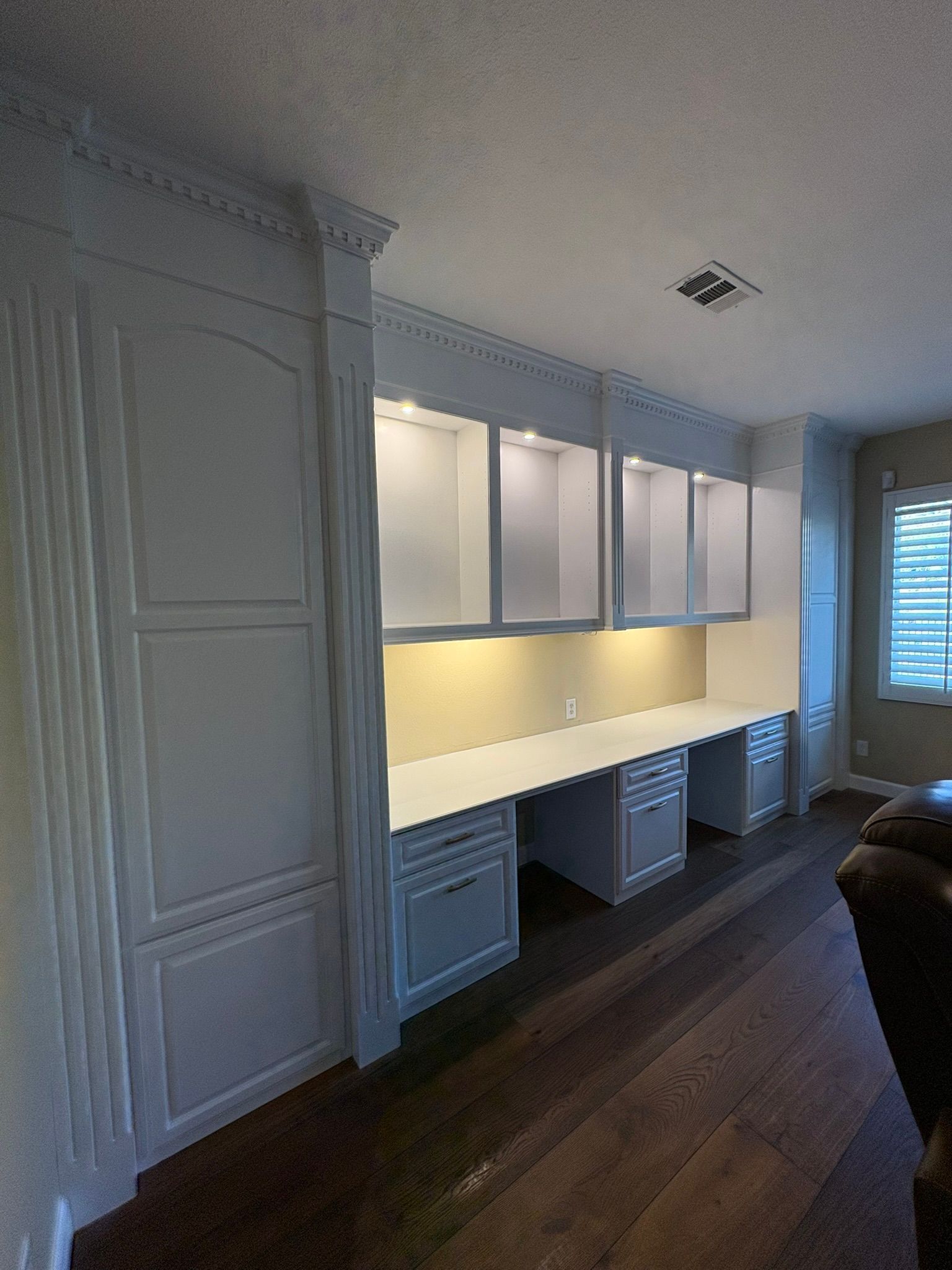 A living room with hardwood floors , white cabinets and a desk.