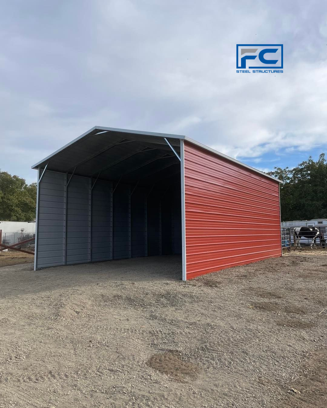 A red barn is sitting in the middle of a gravel lot.