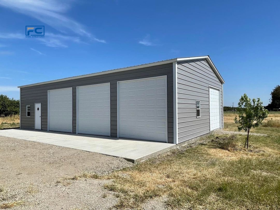 A garage with three garage doors is sitting in the middle of a field.