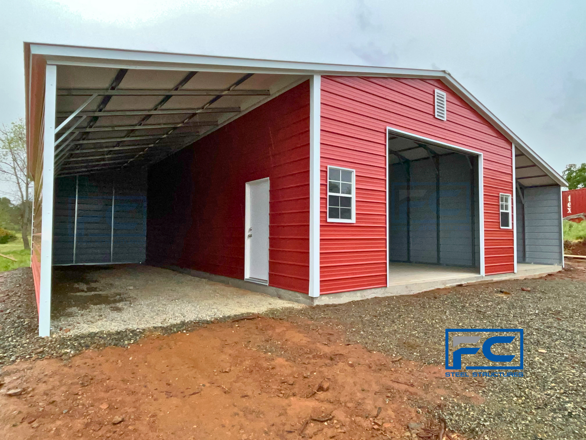 A red barn with a white roof is sitting on top of a dirt field.