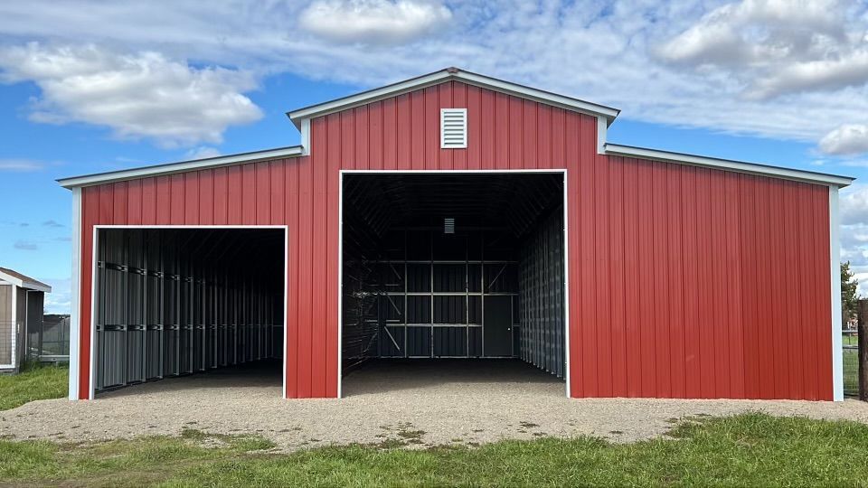 A red barn with two garage doors is sitting in the middle of a grassy field.
