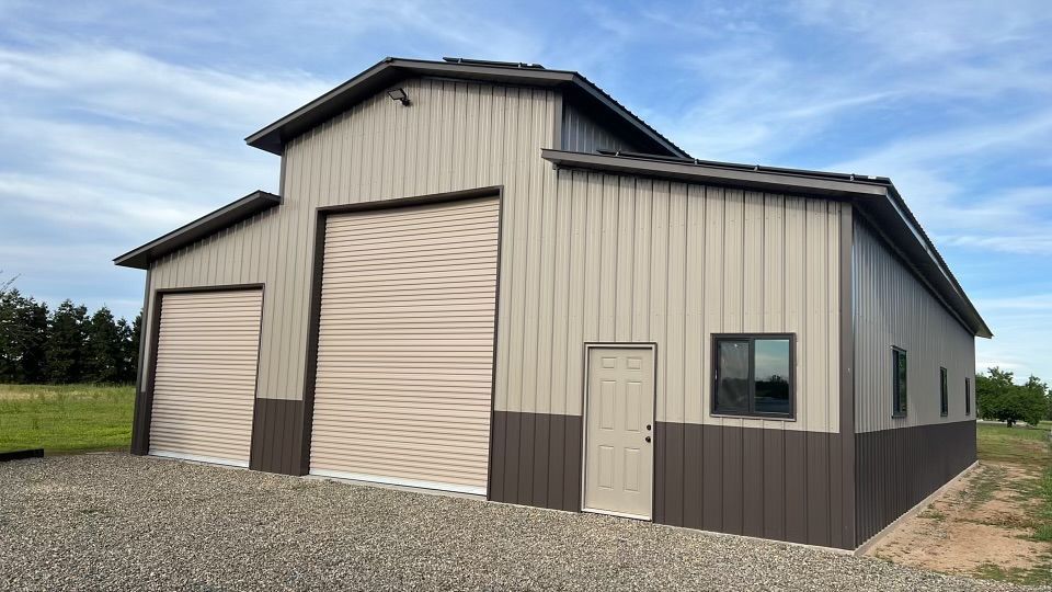 A large metal building with a large garage door is sitting on top of a gravel lot.