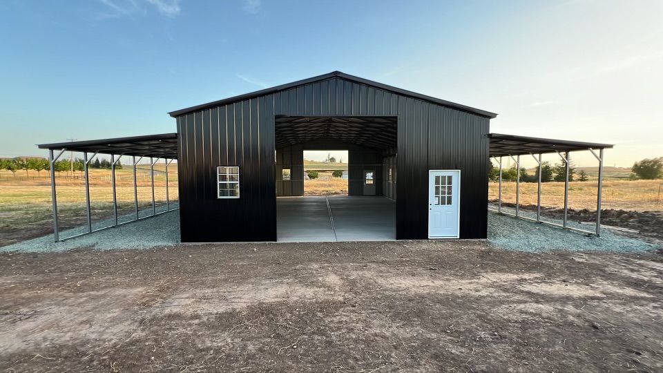 A black metal barn with a white door is sitting in the middle of a dirt field.