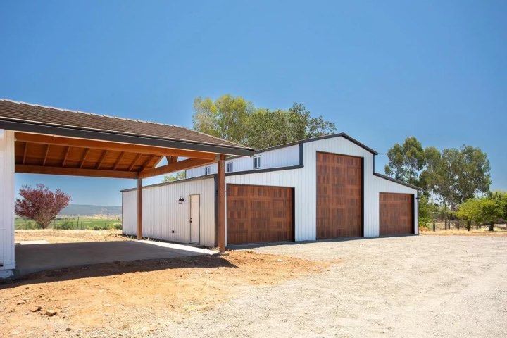 A white building with a wooden garage door and a carport.