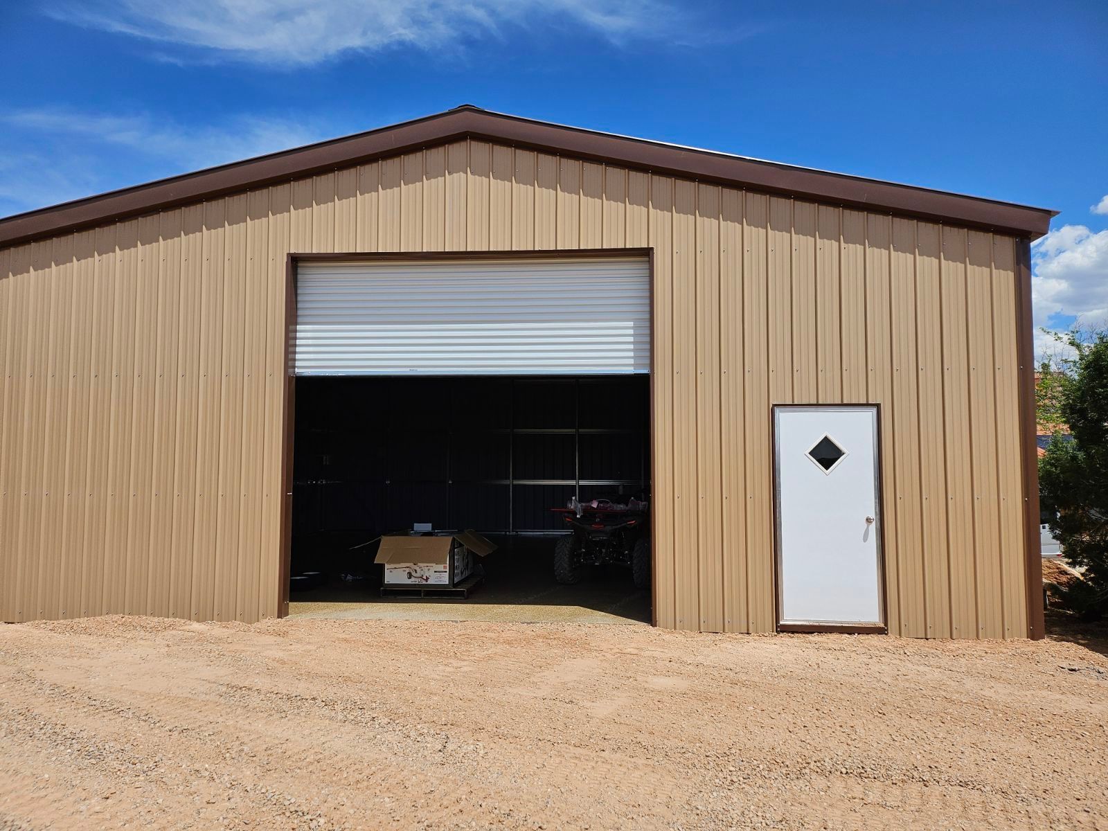 A brown metal building with a white door and a large garage door.