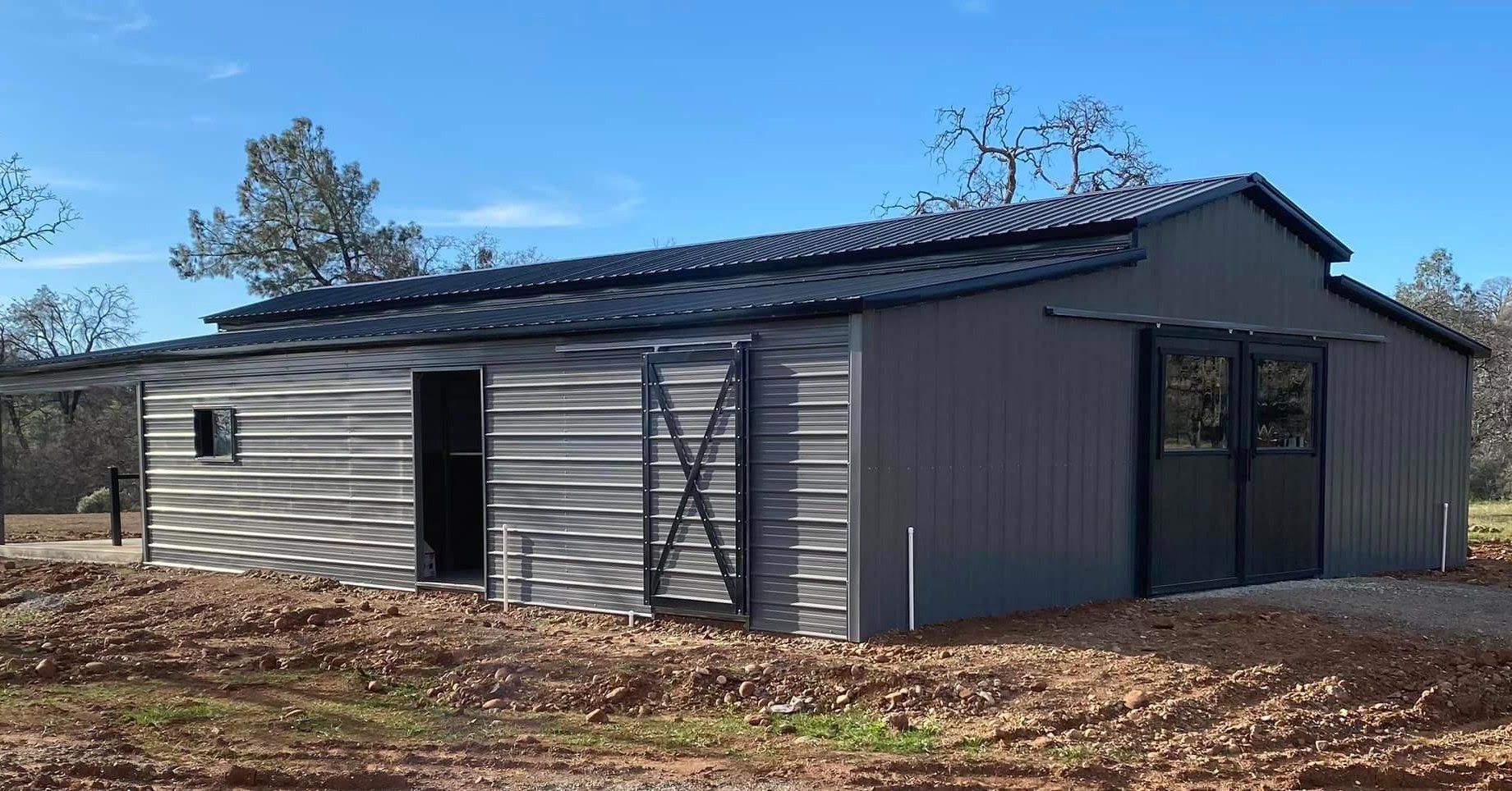 A large metal barn is sitting in the middle of a field.