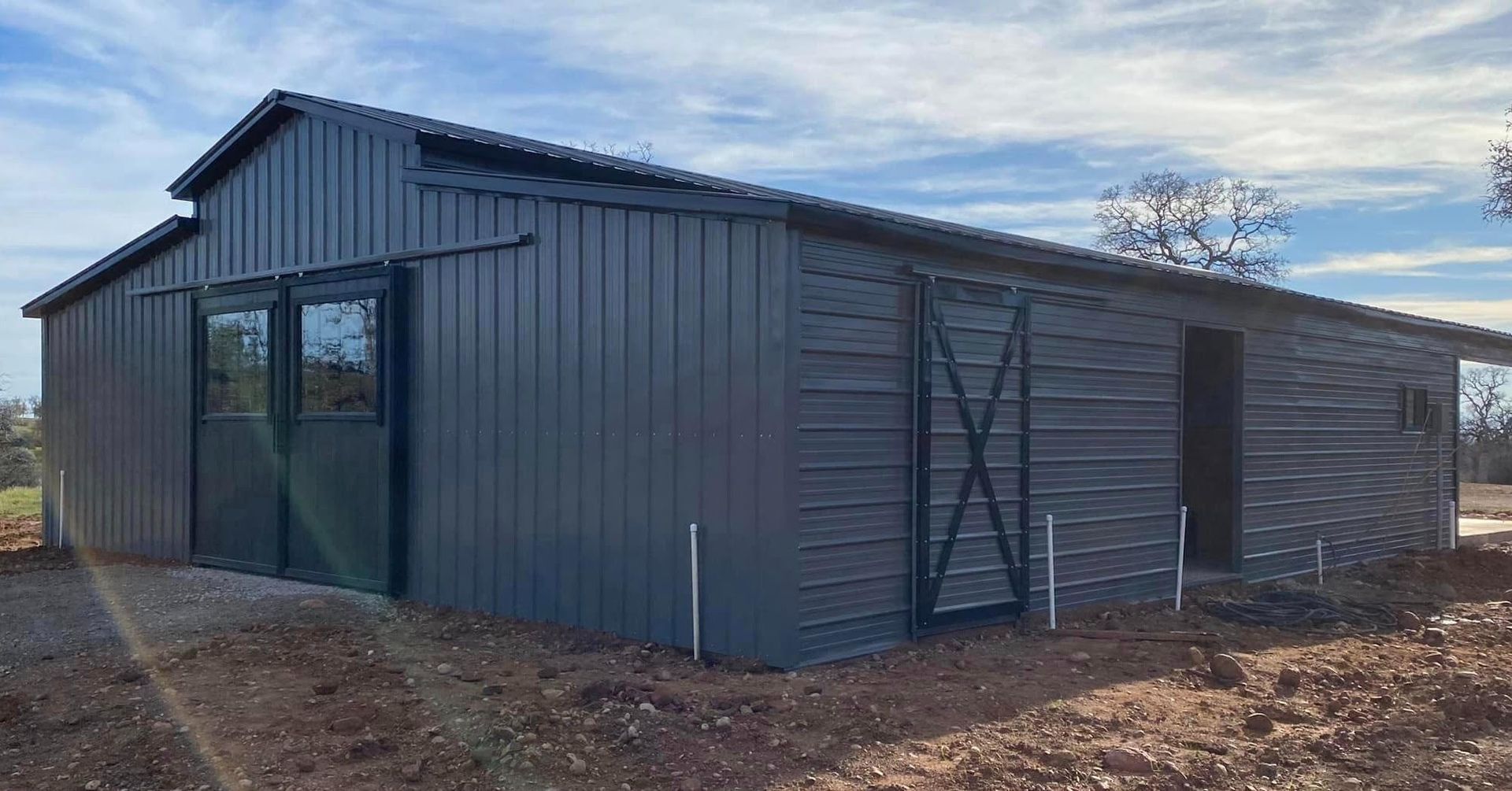 A large black barn is sitting in the middle of a dirt field.
