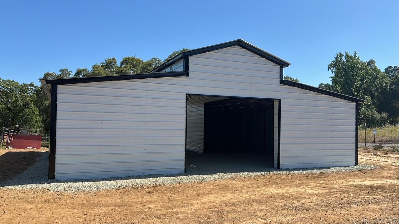 A white barn with a black trim is sitting in the middle of a dirt field.