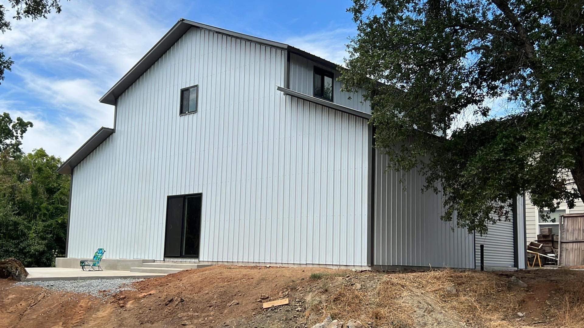 A large white barn is sitting on top of a dirt hill.