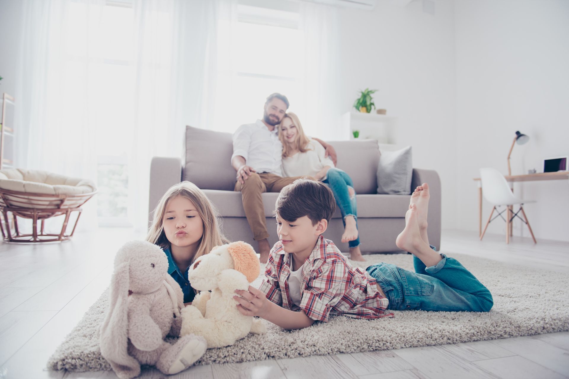 A family is laying on the floor in a living room playing with stuffed animals.