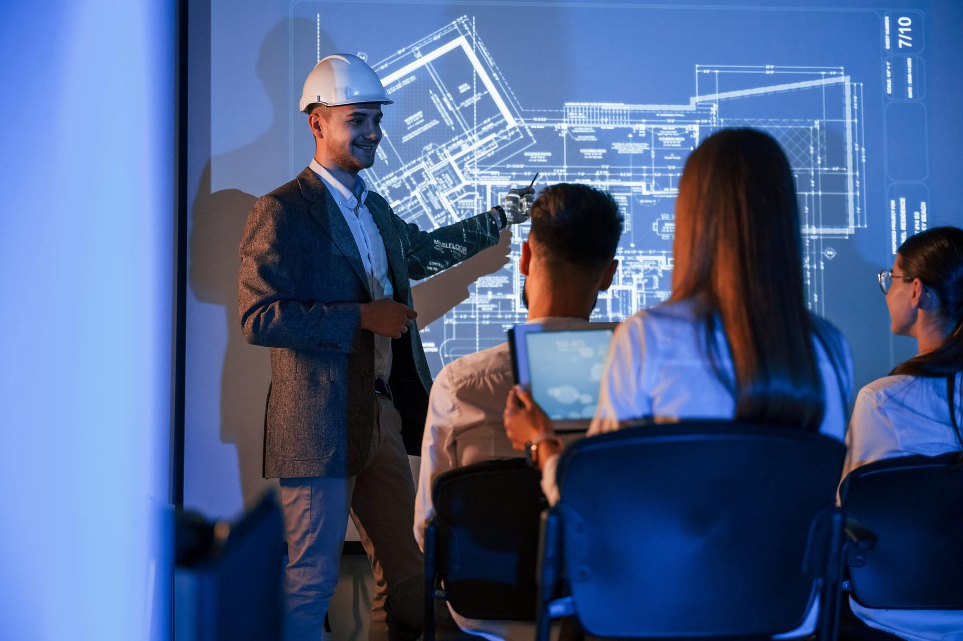 a man in a hard hat is giving a presentation to a group of people .