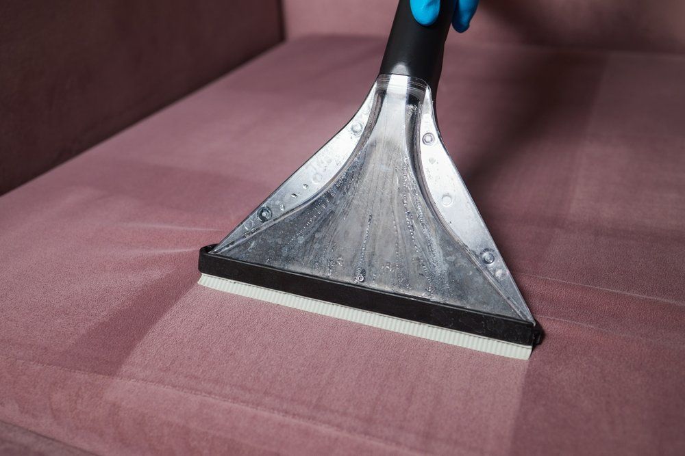 A Person Is Cleaning a Pink Couch with A Vacuum Cleaner — Turbo Clean in Tuncurry, NSW