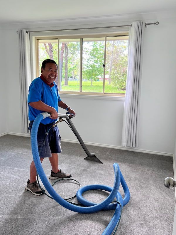 A Man Is Using a Vacuum Cleaner to Clean a Carpet in A Room — Turbo Clean in Tuncurry, NSW