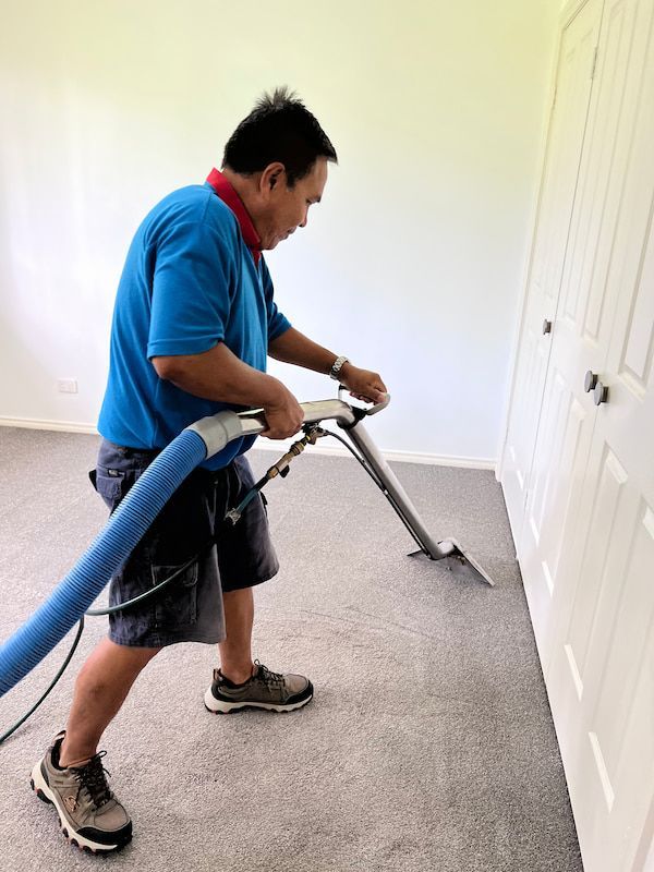 A Man in A Blue Shirt Is Cleaning a Carpet with A Vacuum Cleaner — Turbo Clean in Tuncurry, NSW