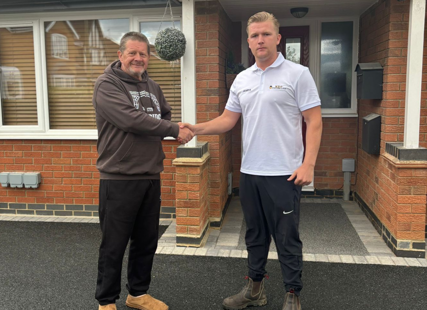Two men shaking hands outside a brick house