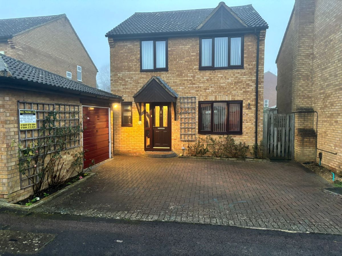 Two-story brick house with lit front doorway and paved driveway at dusk