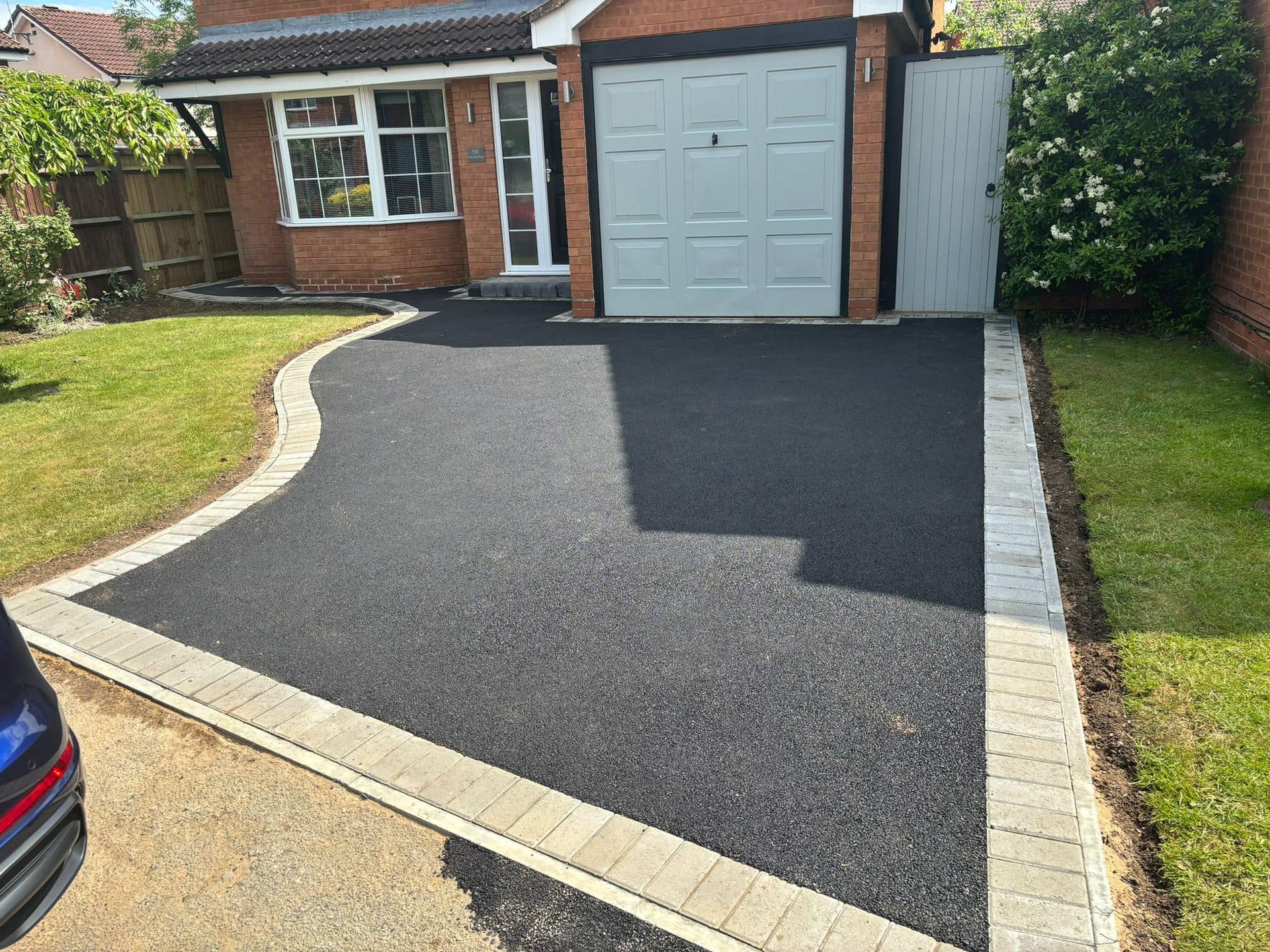 Freshly paved black driveway leading to a brick house with a garage door and front lawn