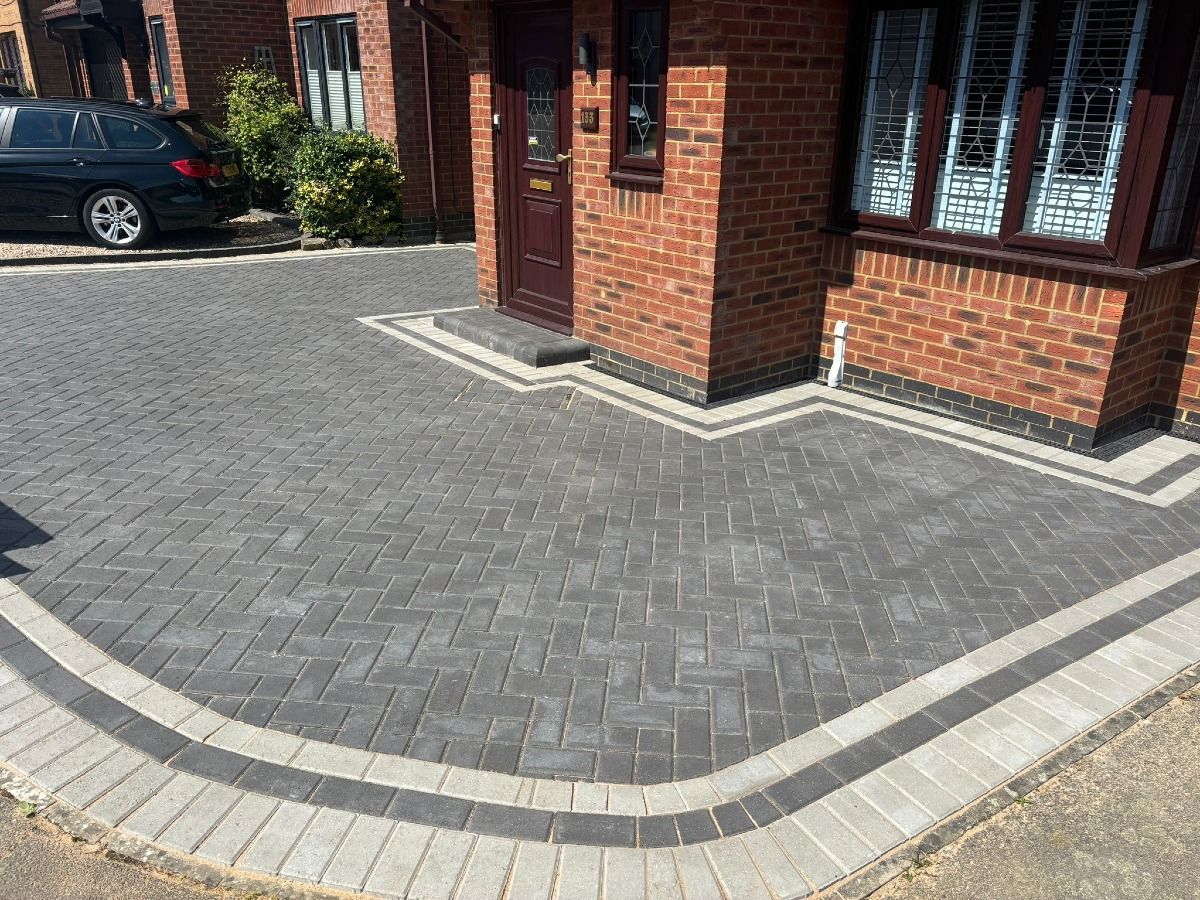Brick-paved driveway and front entrance with a red-brick house, gray edging, and a parked car nearby.