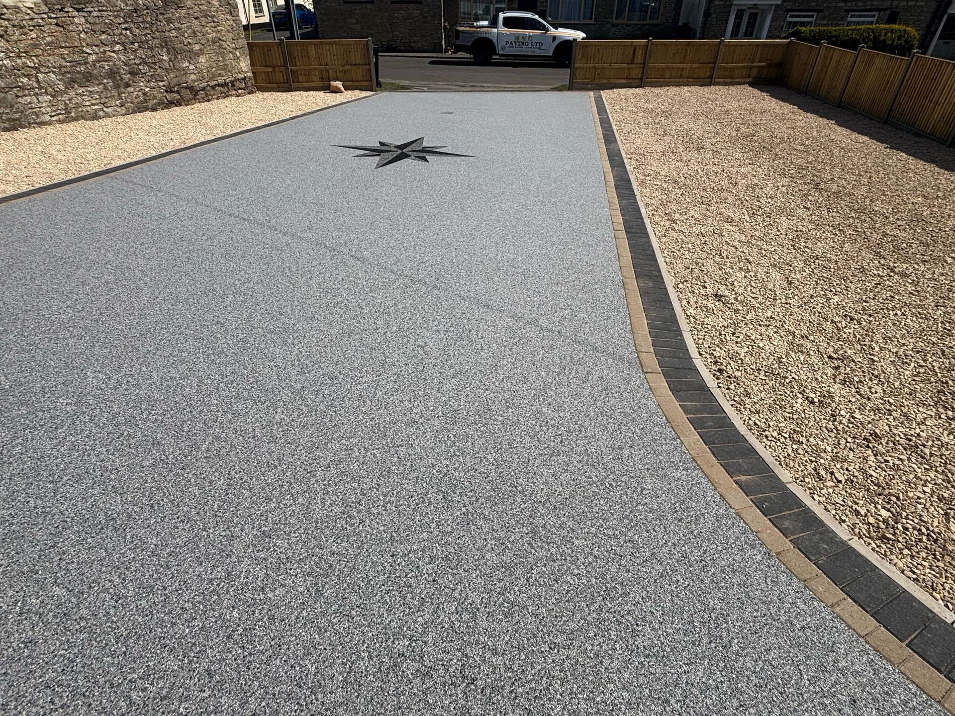 Gravel driveway with a curved border leading to a house entrance and parked car.