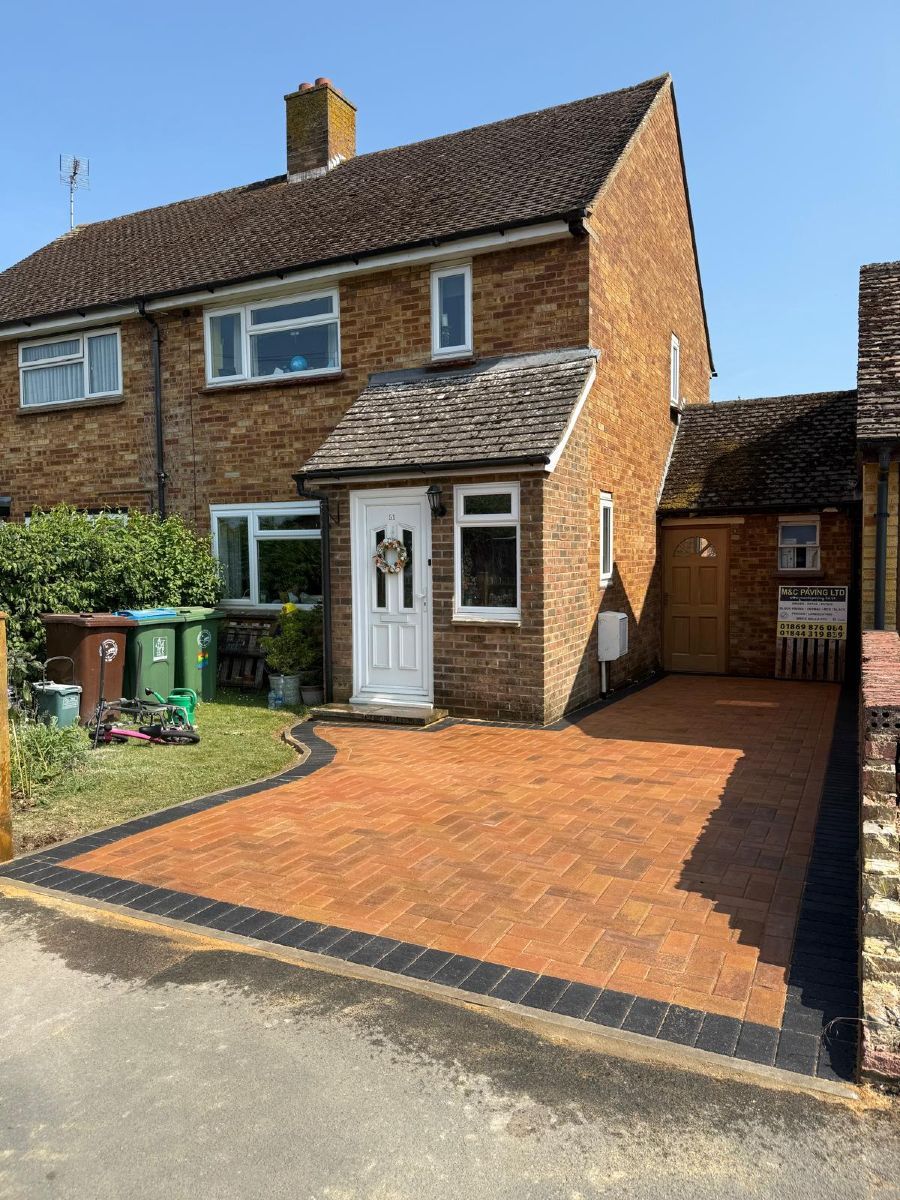 Brick semi-detached house with orange driveway, white front door, and side gate