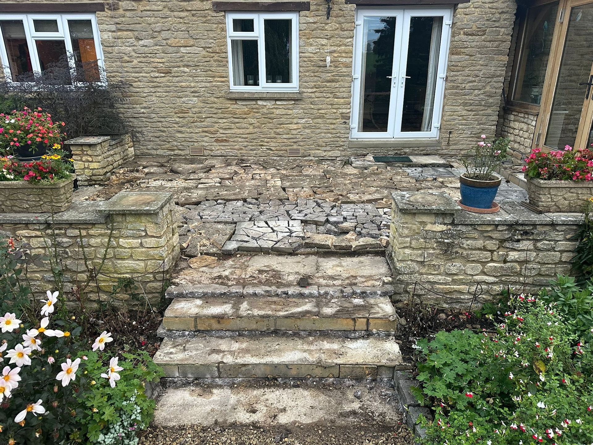 Stone steps leading to a brick house with white-framed windows and garden flowers on both sides