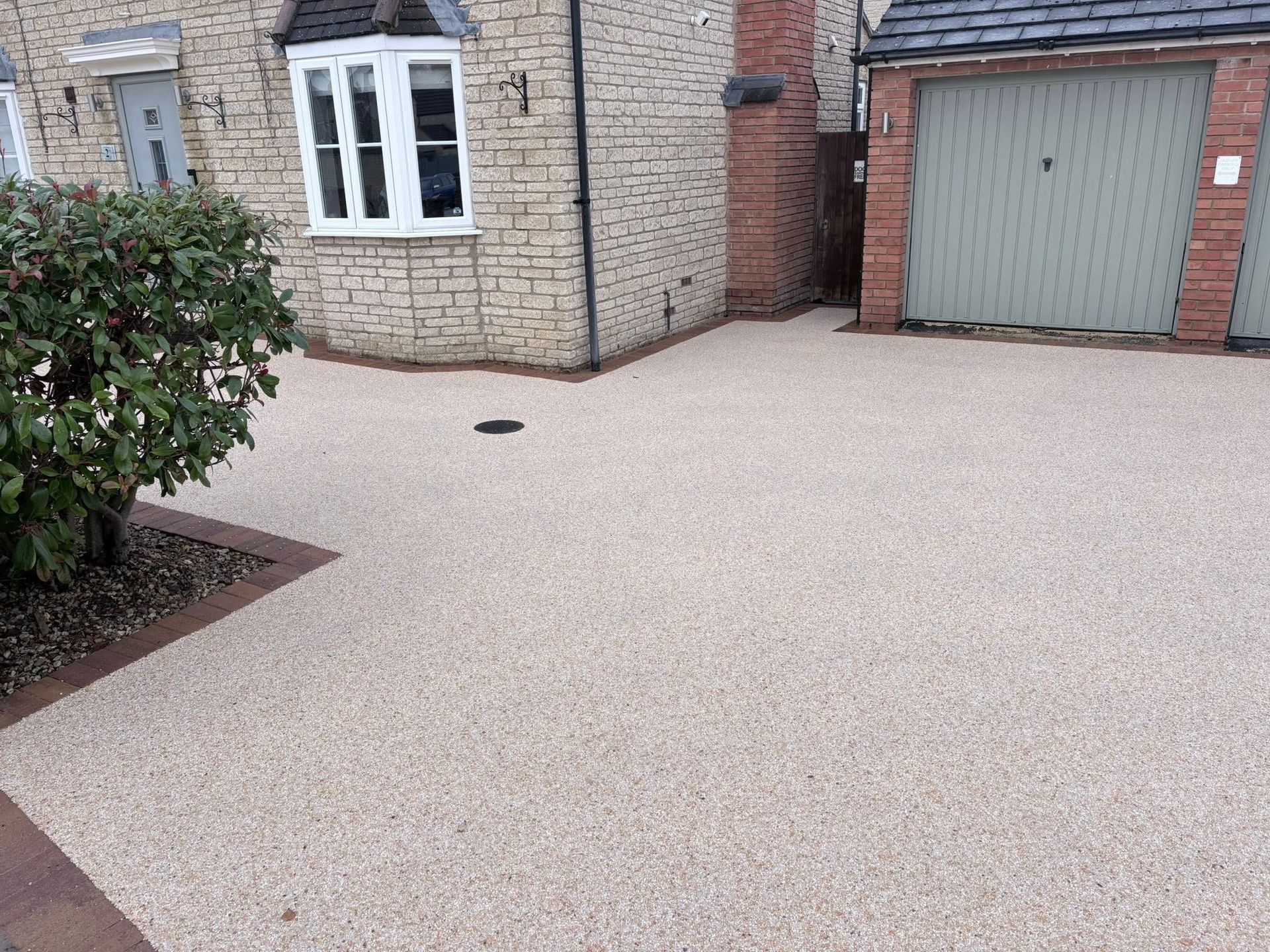 Stone house driveway with pale gravel, garage door, front window, and shrubbery.