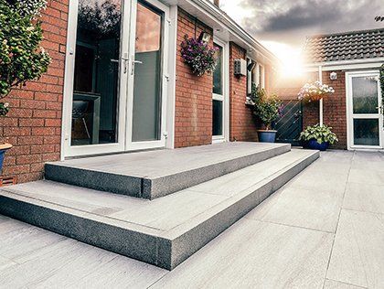 Modern house patio with wide concrete steps, sliding glass doors, and hanging flower baskets at sunset