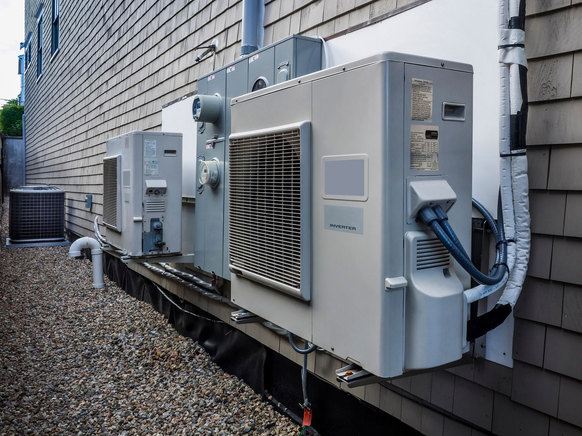 Outdoor HVAC units mounted on a building's side, next to a gravel area.