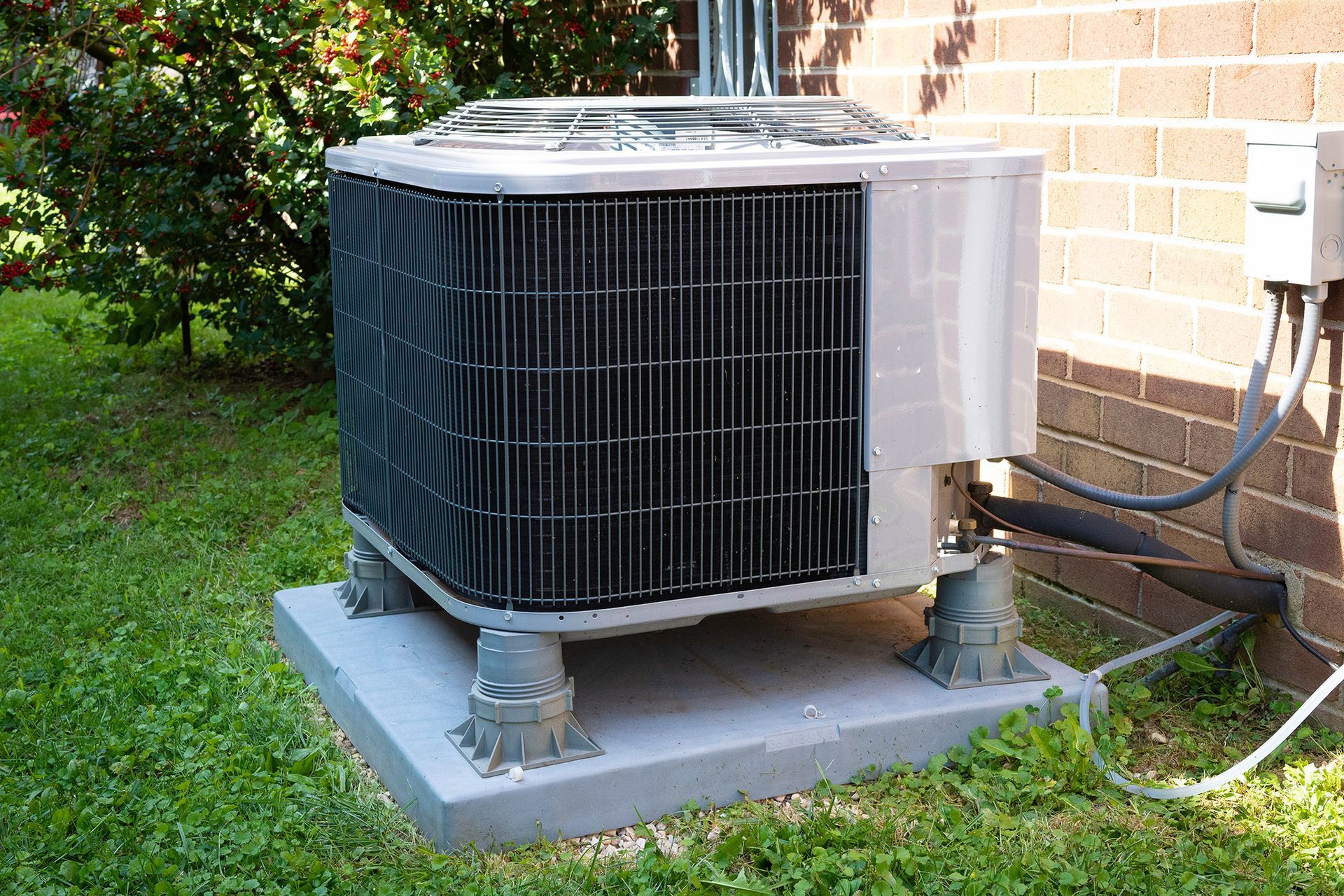AC unit on a concrete pad, on a lawn next to a brick building.