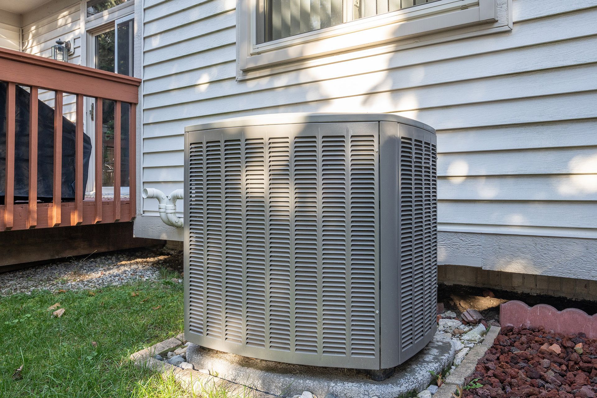 An outdoor air conditioning unit next to a house with a wooden deck and green grass.