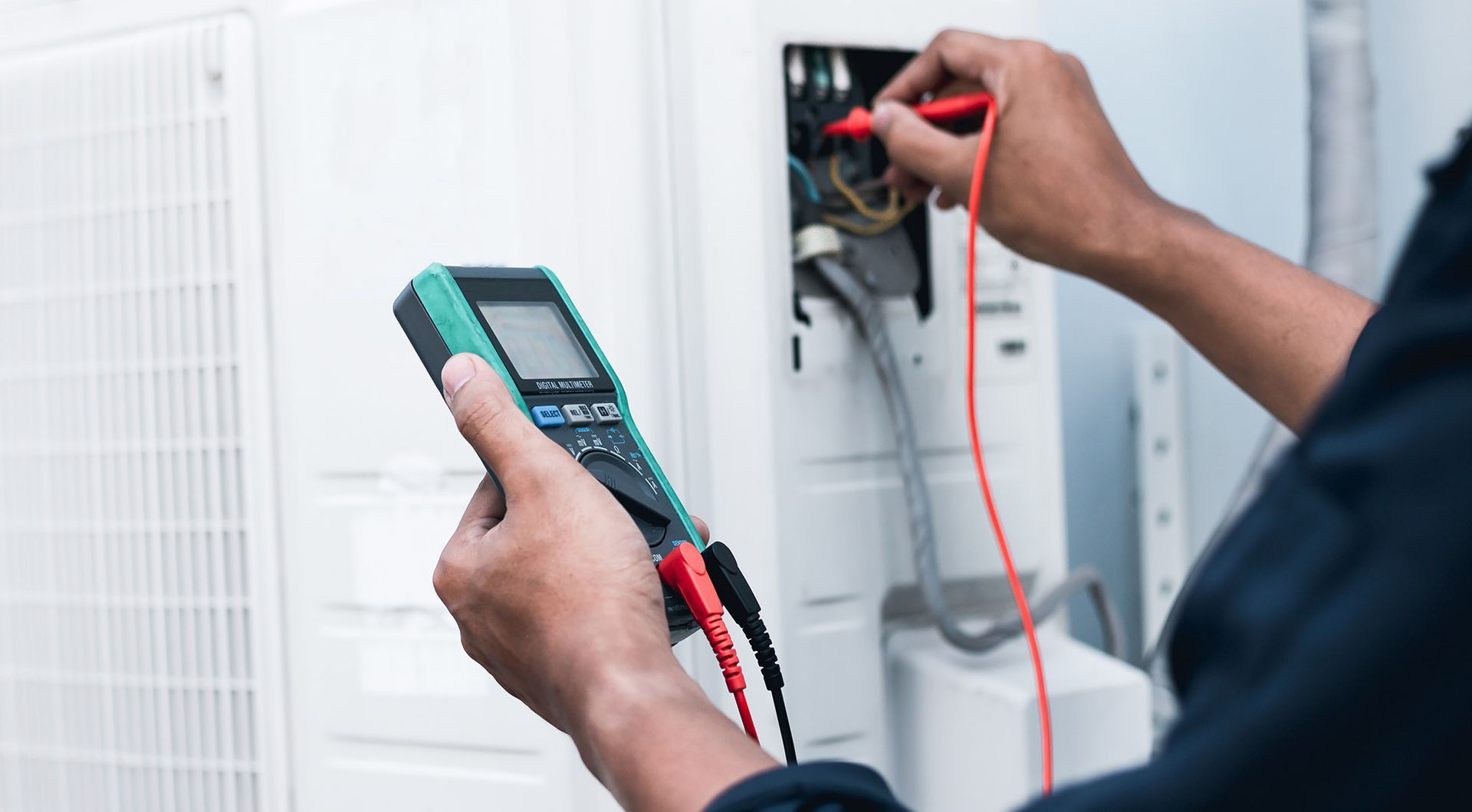 Technician using a multimeter to test electrical components of an air conditioning unit.