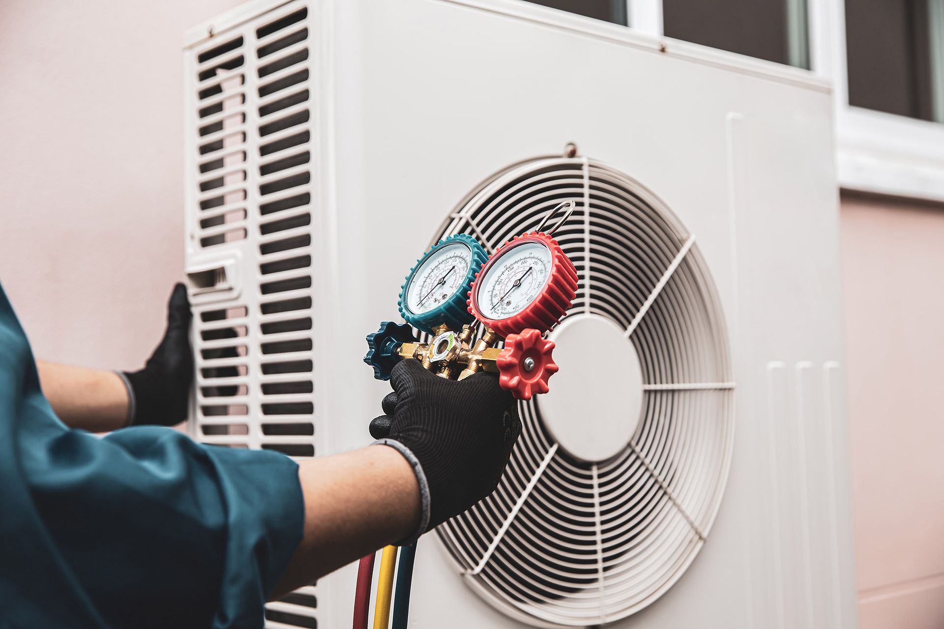 HVAC technician in black gloves using gauges on an outdoor air conditioning unit.