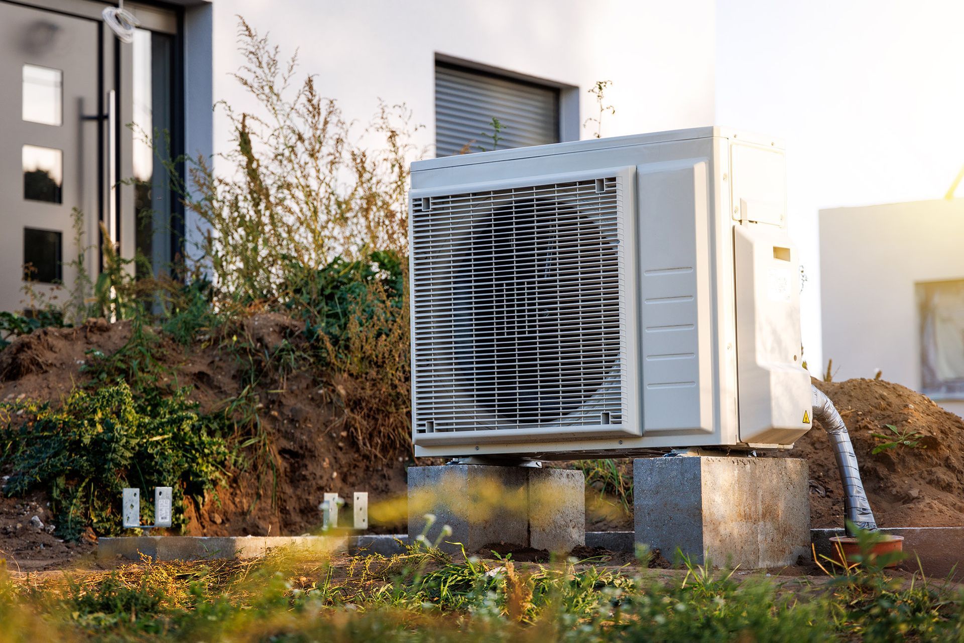 Heat pump unit outside a house on a concrete block, next to some greenery.