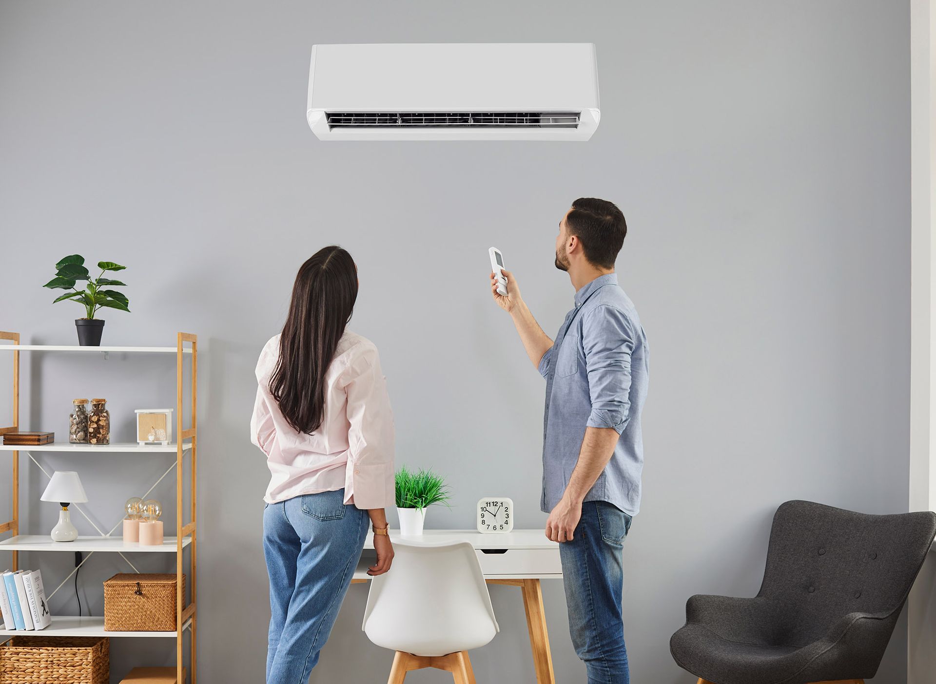 Man using AC remote, with woman, indoors. AC unit above.